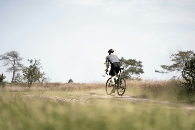 Wielrenner fietst over een onverharde weg in een weids landschap, gericht op uithoudingsvermogenstraining.